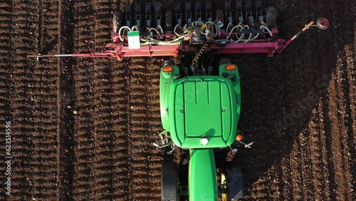 Green tractor tills soil, lays rows for planting potatoes, top view, close-up