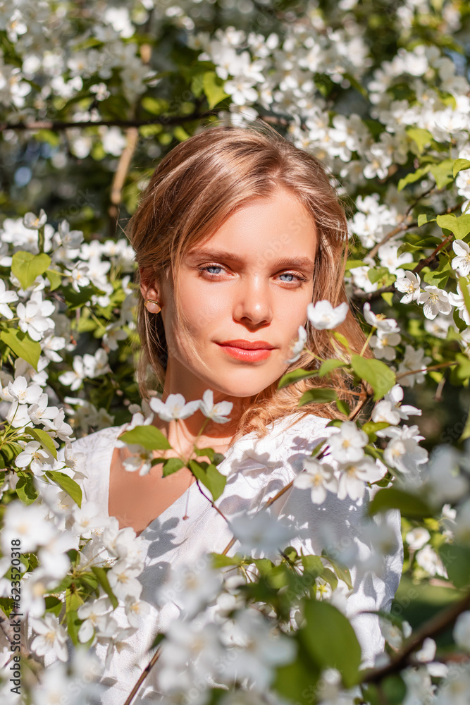 Portrait of a girl in a white dress in blooming apple trees. The girl poses against the background of flowers in the spring park. Portrait of a girl in a white dress in blooming apple trees. The girl poses against the background of flowers in the spring park.