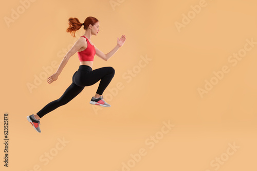 Fototapeta Naklejka Na Ścianę i Meble -  Young woman in sportswear jumping on beige background, space for text