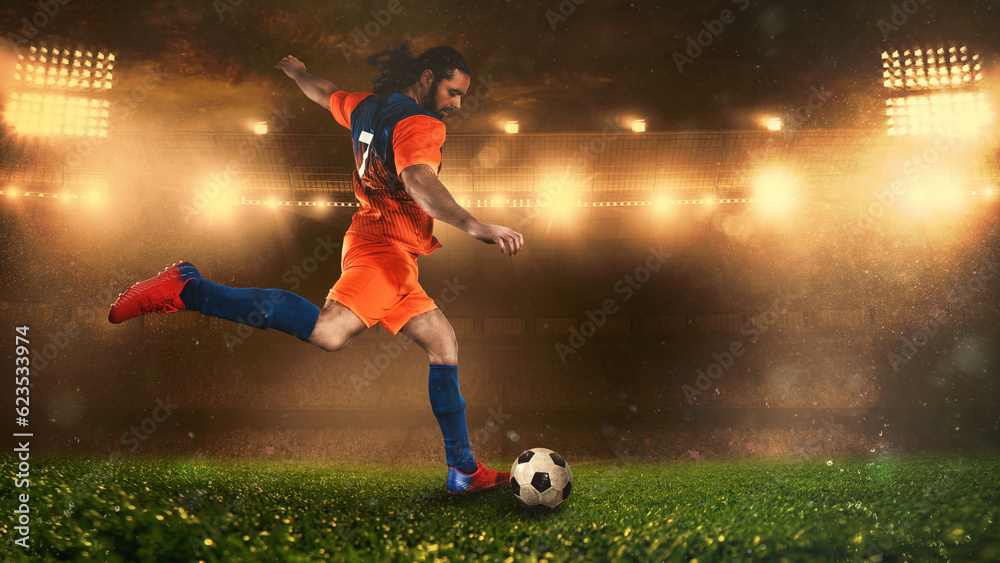Soccer scene at night match with player in a orange uniform kicking the ball with power