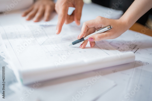 Close-up of a female engineer hand with pink nails and a hand of a male engineer or architect next to him using a pen to write on a blueprint on a table. industrial structure design in office work