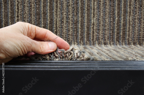 Person showing frayed carpet coming loose on stairstep, stair nosing or stair edging. High traffic staircase with commercial carpet damage by the edge, causing tripping hazard. Selective focus.