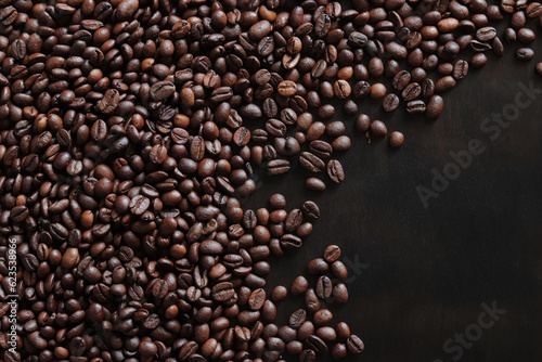 Roasted coffee beans on a wooden dark table, top view. Background of fragrant brown coffee beans scattered over the surface. Copy space