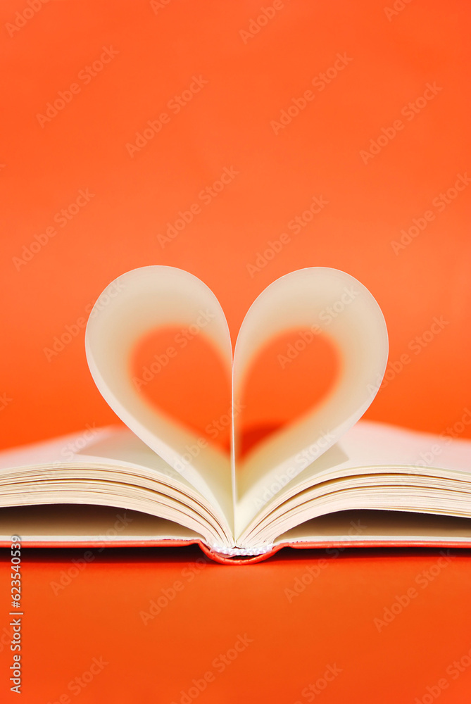 Open book with pages in heart shape on a bright orange background. Poetry Day. Read a book day. Knowledge day. Back to school minimal concept. Space for text. Teachers day. Copy space