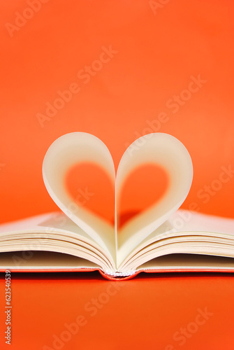 Open book with pages in heart shape on a bright orange background. Book Lovers Day. Knowledge day. Back to school minimal concept. Space for text. Copy space