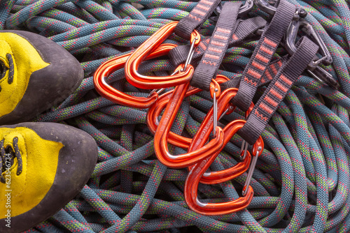 a pair of climbing shoes and a few climbing quickdraws on a background of flaked rope