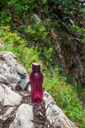 A cherry-colored bottle stands on the rocks in the forest.