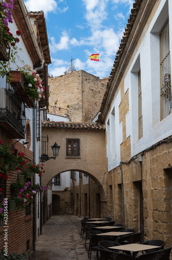 Vista de una callejuela típica con arco y torre con la bandera de España en Baeza, Jaén, Andalucía, España.