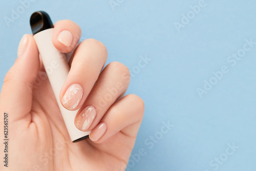 Beautiful womans hand with nude nail design holding electronic cigarette on blue background. Flat lay copy space
