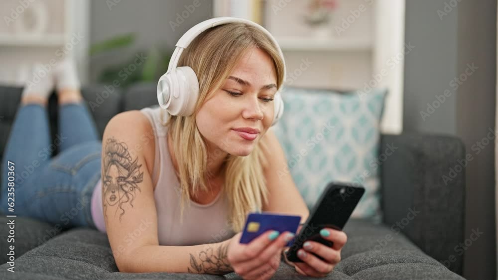 Young blonde woman shopping with smartphone and credit card listening to music at home Young blonde woman shopping with smartphone and credit card listening to music at home