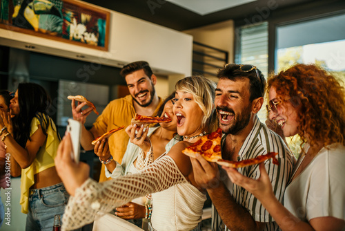 Photography Friends eating a pizza, taking a group selfie and having fun during a house party