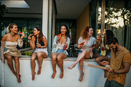 Group of people outdoors sharing stories, jokes, and laughter while enjoying their pizza and drinks, creating a lively and vibrant atmosphere.