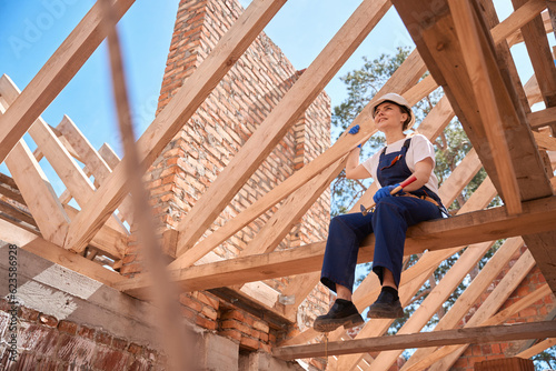 Fotografie Woman roofer sitting on roof beam and enjoying done roofing works