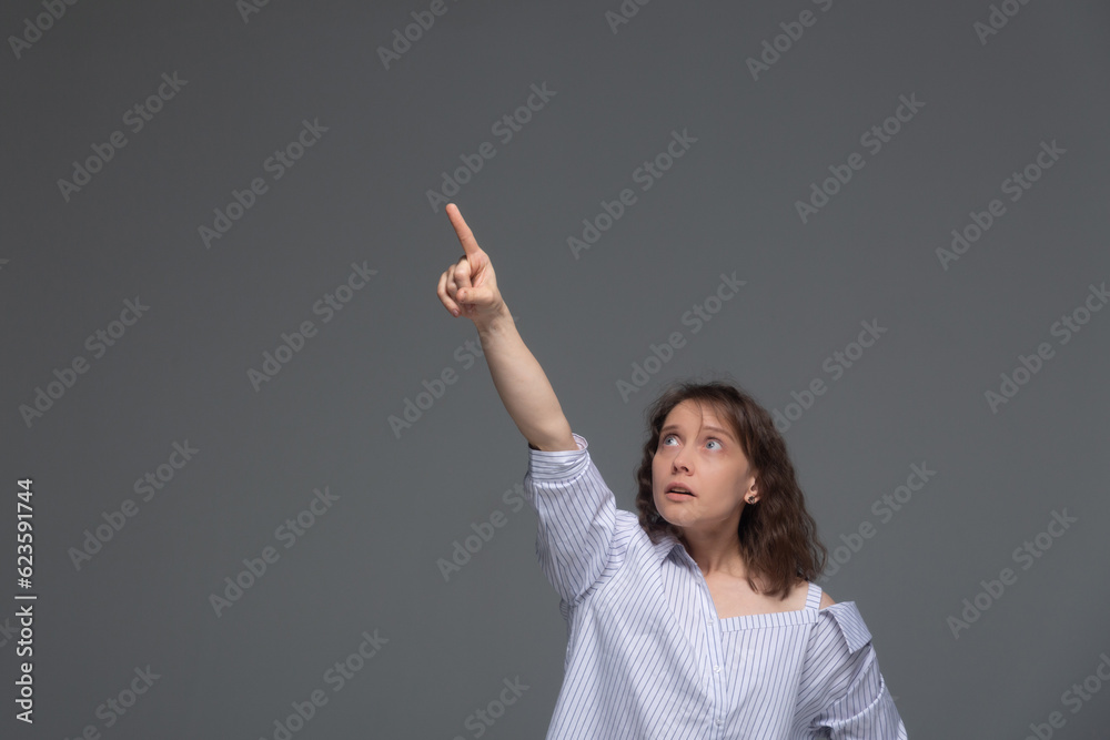 A young woman on a gray background shows her finger up in surprise. A young woman on a gray background shows her finger up in surprise.