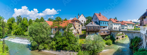 A panorama view across the Selca Sora River towards the weir and fourteenth century Capuchin Bridge in the town of Skofja Loka, Slovenia in summertime photo