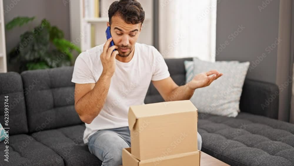 Young hispanic man angry speaking on the phone unpacking cardboard box at home Young hispanic man angry speaking on the phone unpacking cardboard box at home