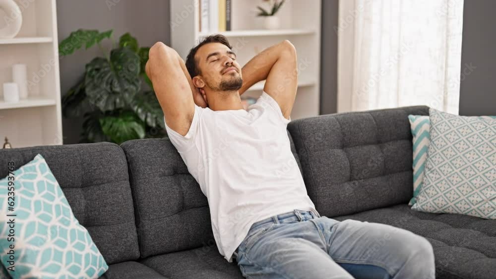 Young hispanic man relaxed with hands on head sitting on sofa at home Young hispanic man relaxed with hands on head sitting on sofa at home