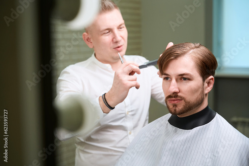 Handsome barber doing his work in modern salon