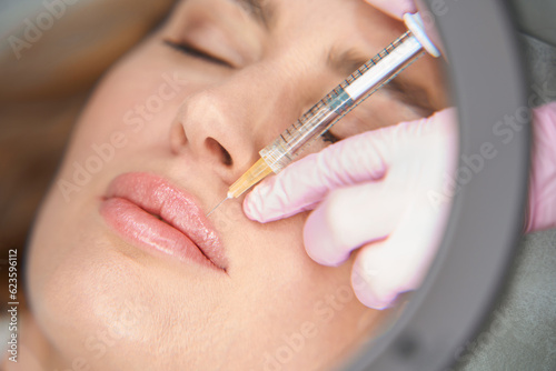 Esthetician makes injections to the woman in the nasolabial fold