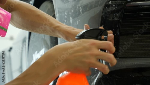 Close up of paint protection film installation on front bumper of modern luxury car. PPF is polyurethane film applied to car surface to protect the paint from stone chips, bug splatter, and abrasion.