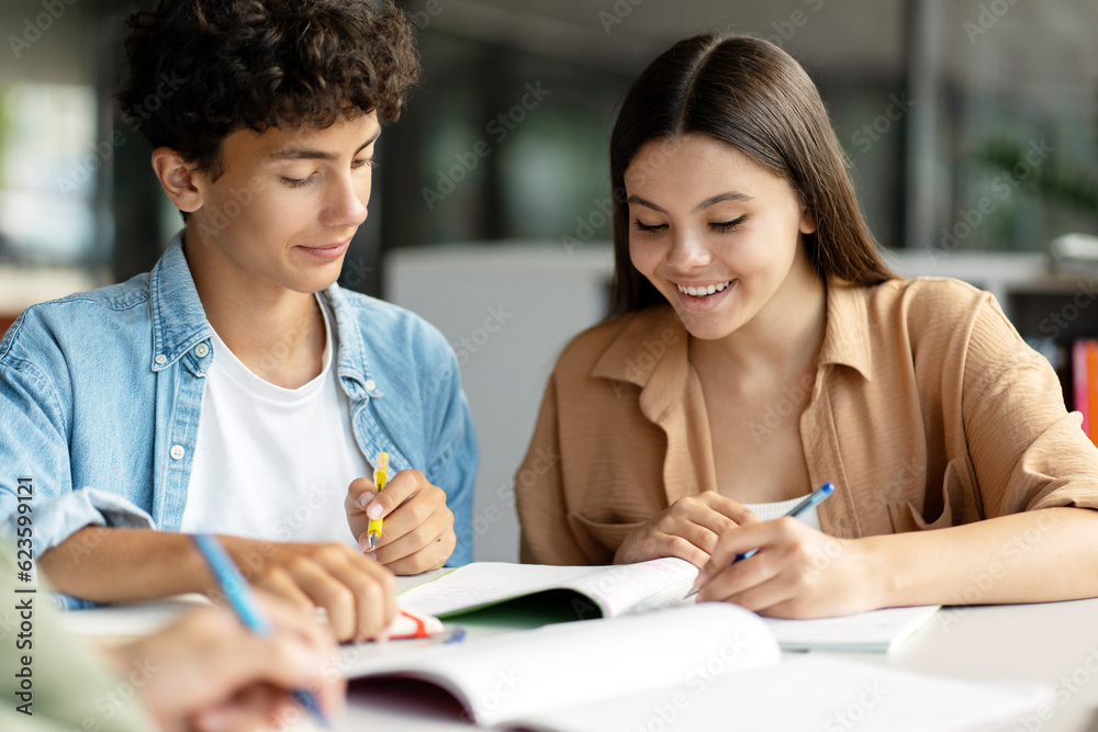 Portrait of school girl and boy studying together, learning language, exam preparation sitting in modern classroom. Back to school, lesson, education concept Portrait of school girl and boy studying together, learning language, exam preparation sitting in modern classroom. Back to school, lesson, education concept