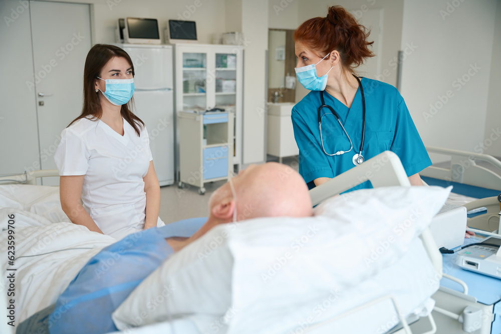 Obraz premium Female anesthetist and surgeon communicating with elderly patient at clinic