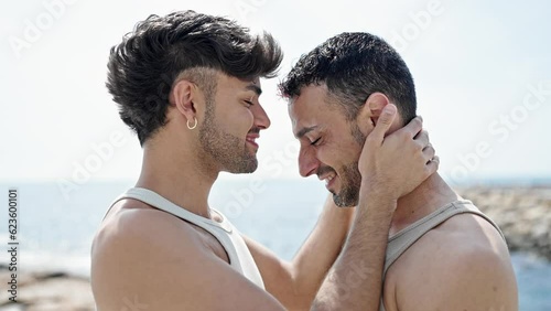 Two men couple standing together kissing at seaside