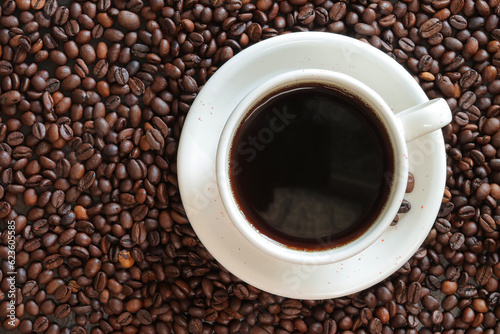 A cup of black coffee with scattered roasted coffee bean, top view. Americano coffee. Top view of a cup of coffee on the background of roasted coffee beans