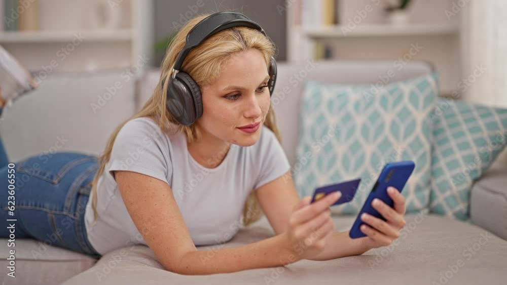Young blonde woman shopping with smartphone and credit card listing to music at home Young blonde woman shopping with smartphone and credit card listing to music at home
