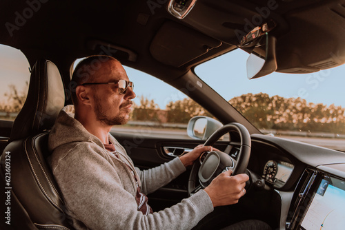 A man with a sunglasses driving a car at sunset. The concept of car travel