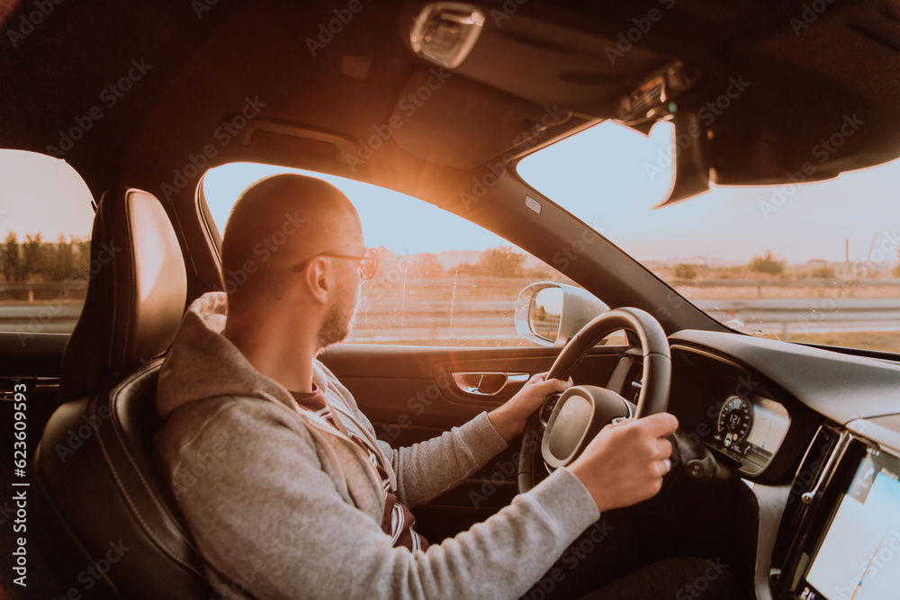 A man with a sunglasses driving a car at sunset. The concept of car travel