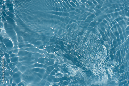 Blue water with ripples on the surface. Defocus blurred transparent blue colored clear calm water surface texture with splashes and bubbles. Water waves with shining pattern texture background.