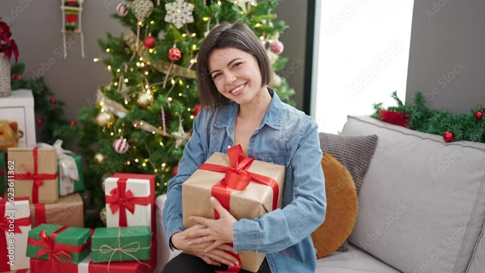 Young caucasian woman holding christmas gift sitting on the sofa at home Young caucasian woman holding christmas gift sitting on the sofa at home