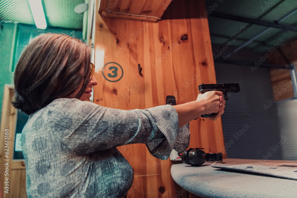 A woman practices shooting a pistol in a shooting range while wearing protective headphones