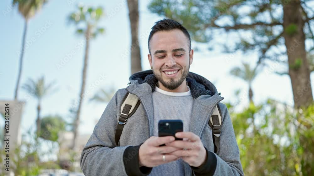 Hispanic man using smartphone smiling at the park Hispanic man using smartphone smiling at the park