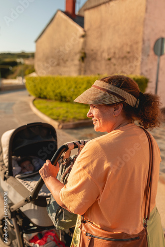 A young grandmother happily strolls her baby granddaughter, just a few months old, in her stroller during a sunny summer afternoon in a small village in northern Galicia, Spain