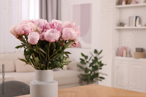 Vase with pink peonies on wooden table in dining room. Space for text