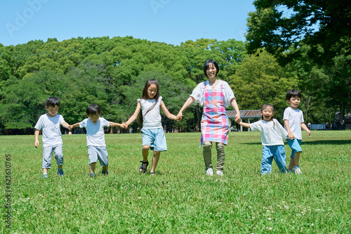 緑地で手を繋いで並ぶ子どもたちと女性