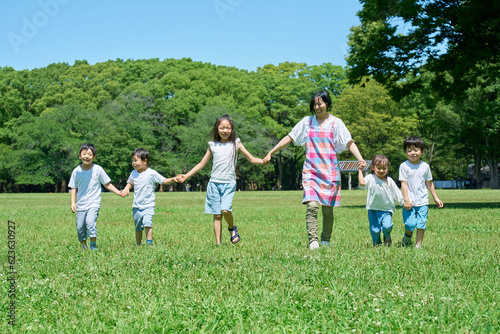 緑地で手を繋いで並ぶ子どもたちと女性