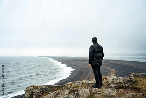 Man looking out at the black sand of Hvalnes Beach photo