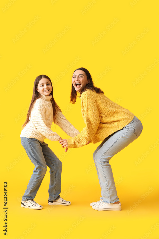 Fototapeta premium Little girl and her mother in knitted sweaters dancing on yellow background