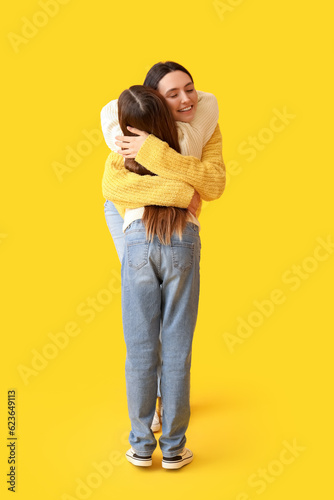 Little girl and her mother in knitted sweaters hugging on yellow background © Pixel-Shot