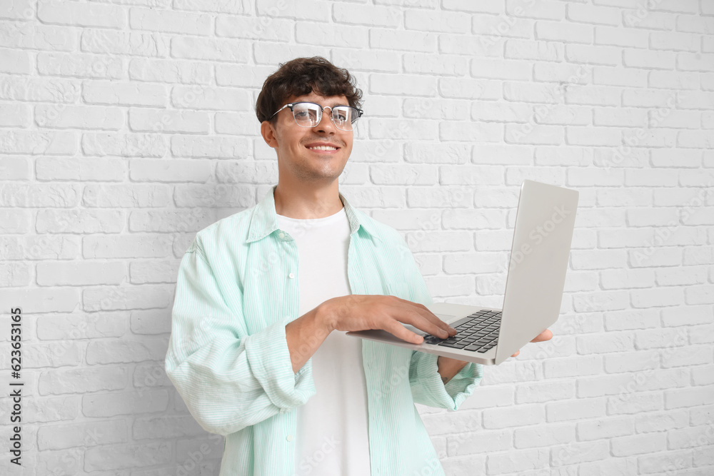 Male programmer working with laptop on white brick background Male programmer working with laptop on white brick background
