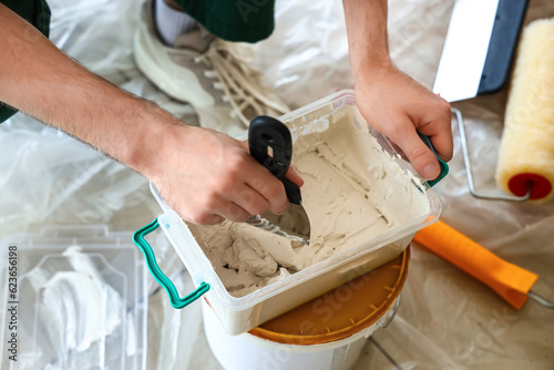 Male worker with putty knife and plaster working in room, closeup