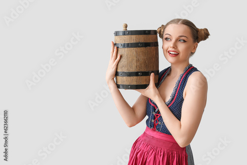 Beautiful Octoberfest waitress with barrel of beer on light background