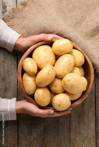 Woman holding bowl with raw potatoes on wooden background