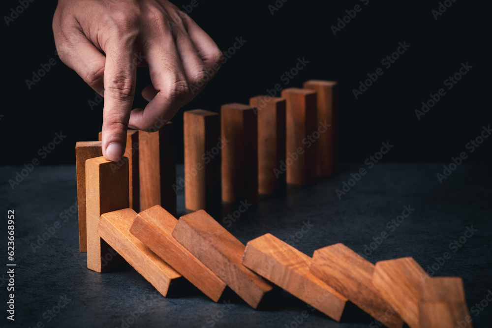 Close up of businessman hand Stopping Falling wooden Dominoes effect from continuous toppled or risk, strategy and successful intervention concept for business solution and problem.