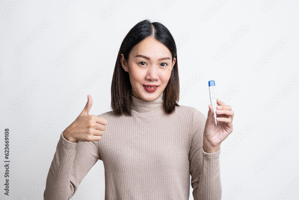 Portrait of beautiful happy young asian woman over isolated white background holding thermometer and feeling better after cold, thumb up and smiling to camera,got rid of fever, has normal temperature. Portrait of beautiful happy young asian woman over isolated white background holding thermometer and feeling better after cold, thumb up and smiling to camera,got rid of fever, has normal temperature.
