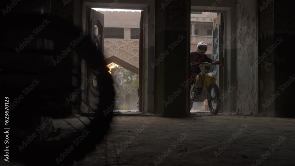 Two bikers on sports bikes and protective suits drive into a dark old building Two bikers on sports bikes and protective suits drive into a dark old building