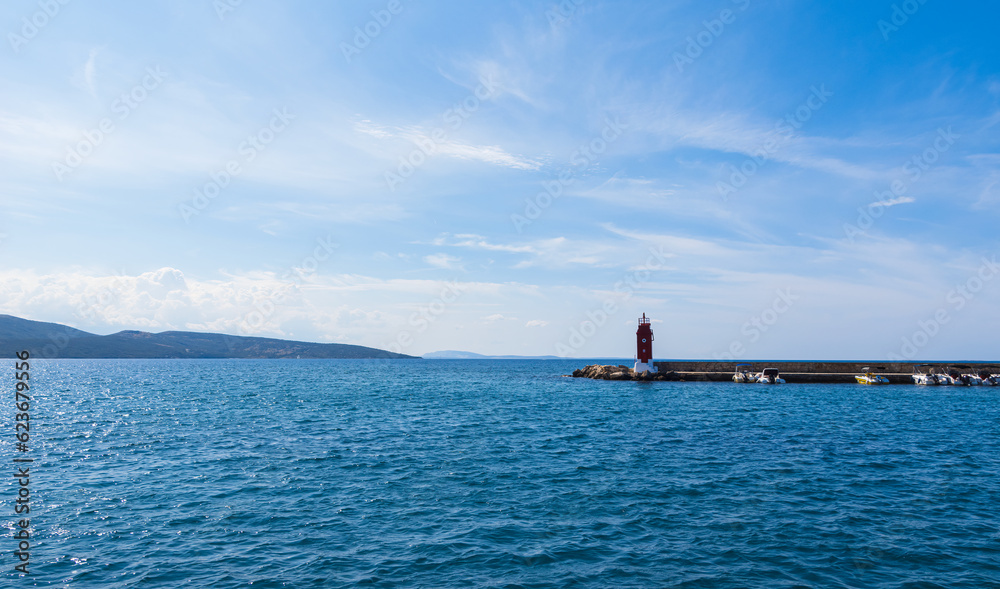 Red lighthouse on sea with ship in city harbor Krk, Croatia